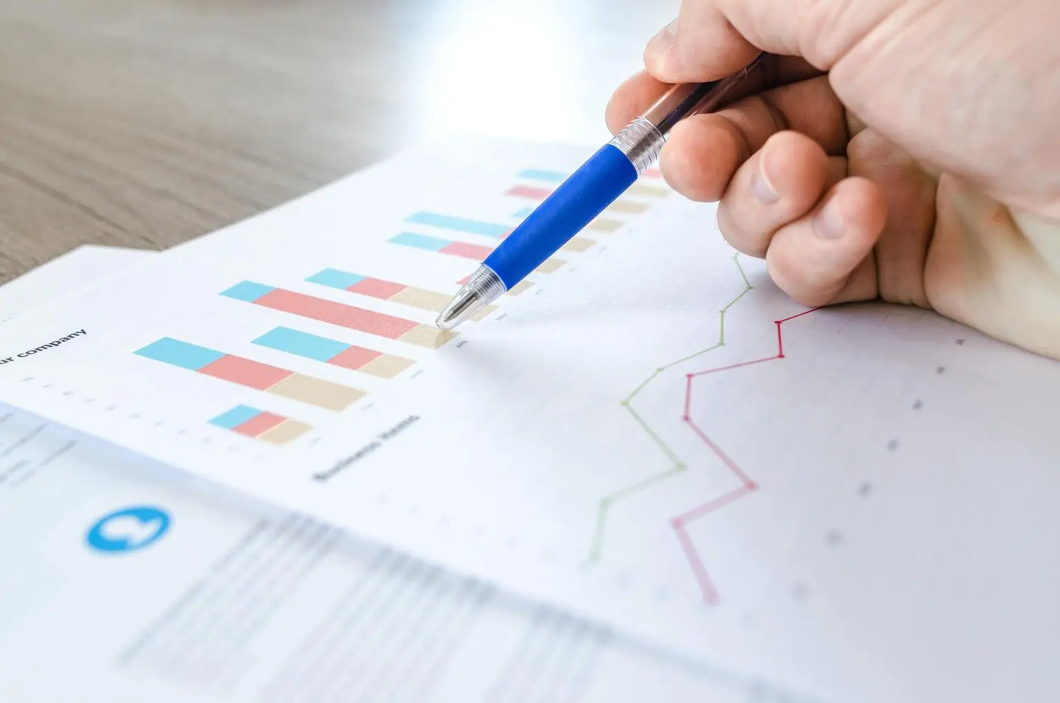 Image of printout of stacked bar chart and line charts and person annotating paper with pen