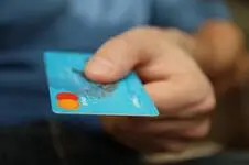 A hand holding a credit card as if they are about to push it into an ATM