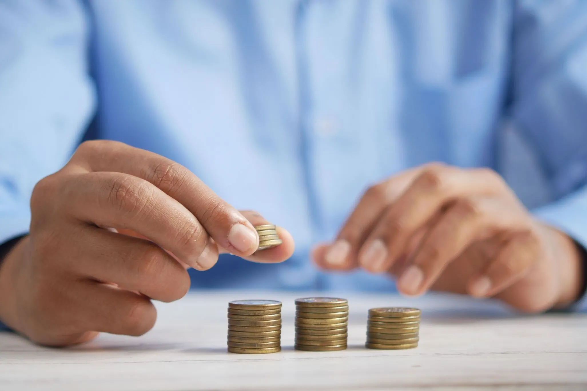 Stacks of coins from right-to-left in increase heights and hand adding four more coins to the left most stack.